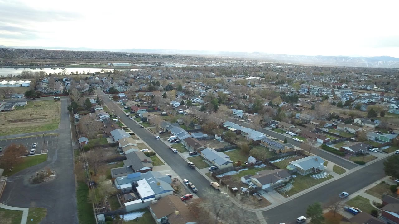 Aerial view of suburban streets, homes, parking lot, fields, and distant water.