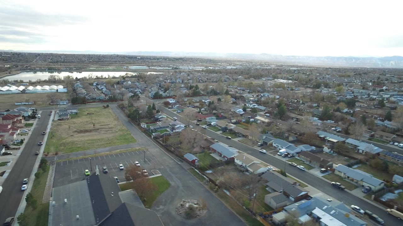 Aerial view of suburban streets, homes, parking lot, and distant water.