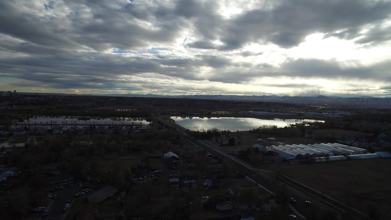 Aerial view of dark land, reflective water, roads, and heavy clouds.