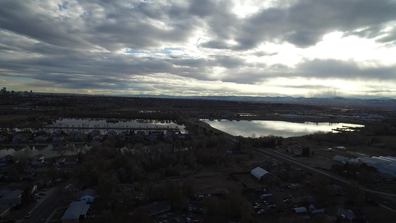 Wide aerial view of wetlands, houses, roads, distant skyline, and heavy dusk clouds.