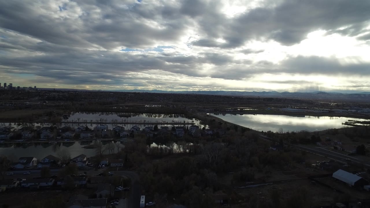 Wide aerial view of marsh ponds under heavy clouds at dusk.
