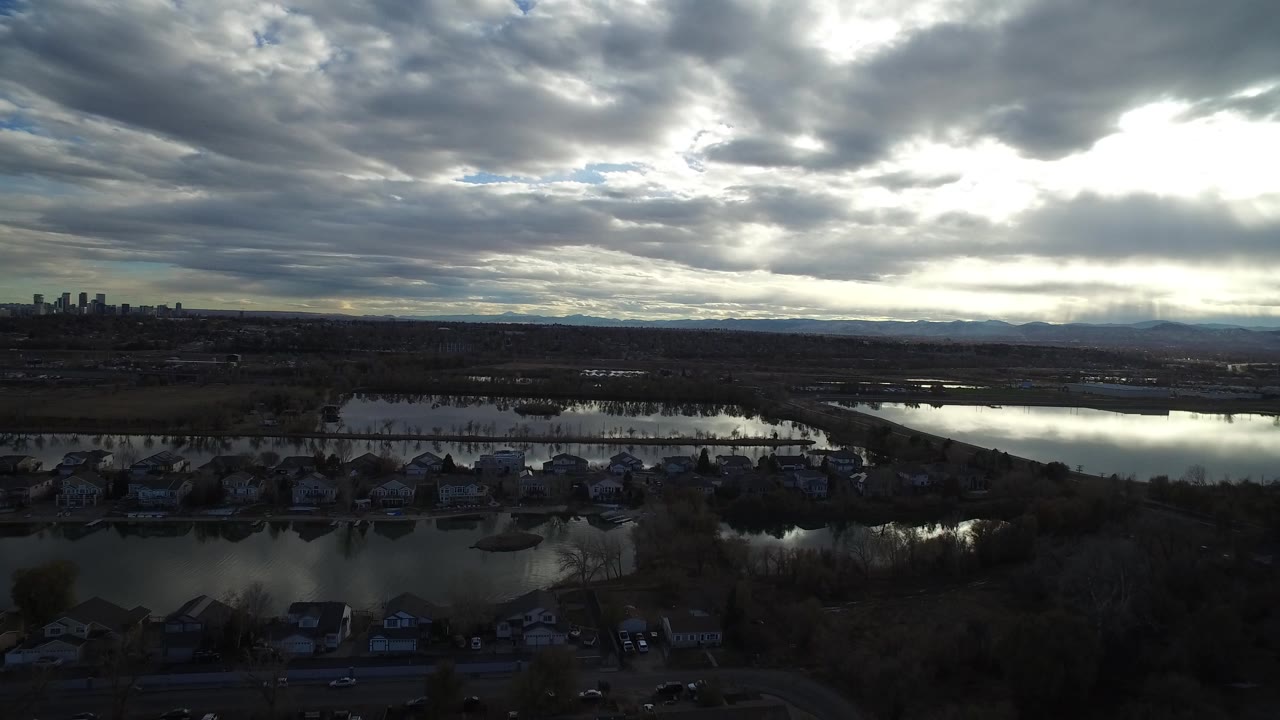 Aerial view of a lake, shoreline houses, wetlands, distant skyline, and heavy clouds.