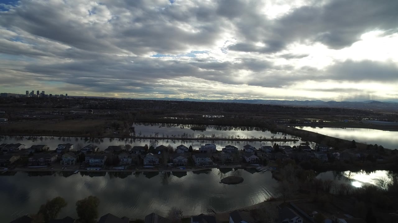 Westminster, Colorado aerial view looking over shoreline homes and reflective lakes toward a small distant skyline under layered clouds, with no visible people.