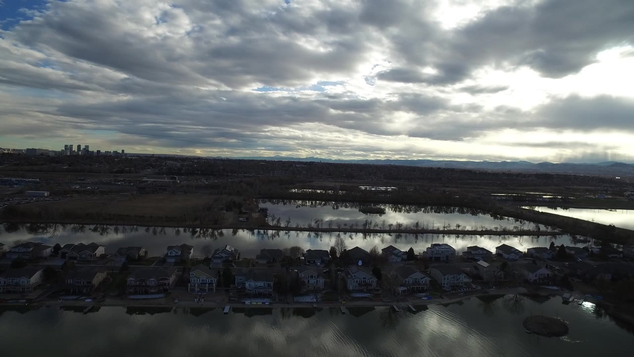 Aerial view of homes, water channels, open land, skyline, mountains, and cloudy sky.