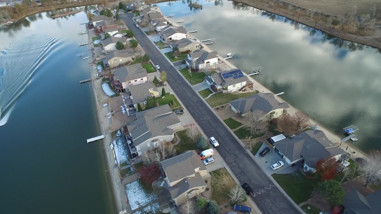 Aerial view of waterfront houses along a residential street with a boat wake on the left.