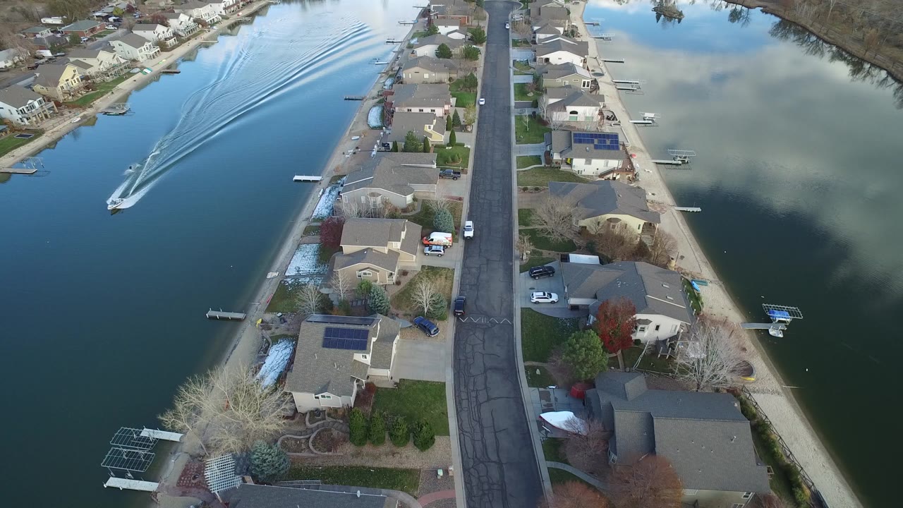 Aerial view in Westminster, Colorado showing houses and a straight residential road between two calm lake arms, with a small motorboat wake at left and no visible people.