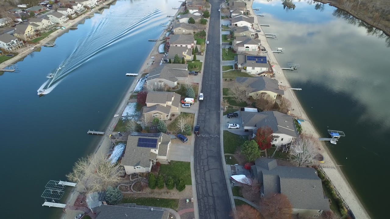 Aerial neighborhood view with homes, docks, and still water reflecting clouds.
