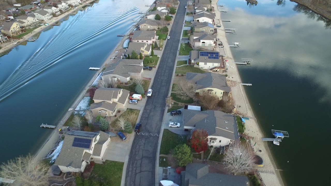 Aerial view of waterfront homes, a residential street, docks, and blue-green water.