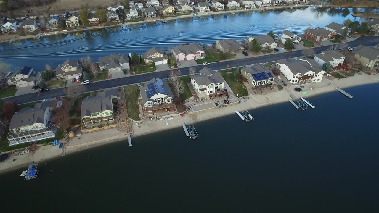 Aerial view in Westminster, Colorado with dark lake water in the foreground, waterfront homes and small docks along the shore, and a road behind the beach.