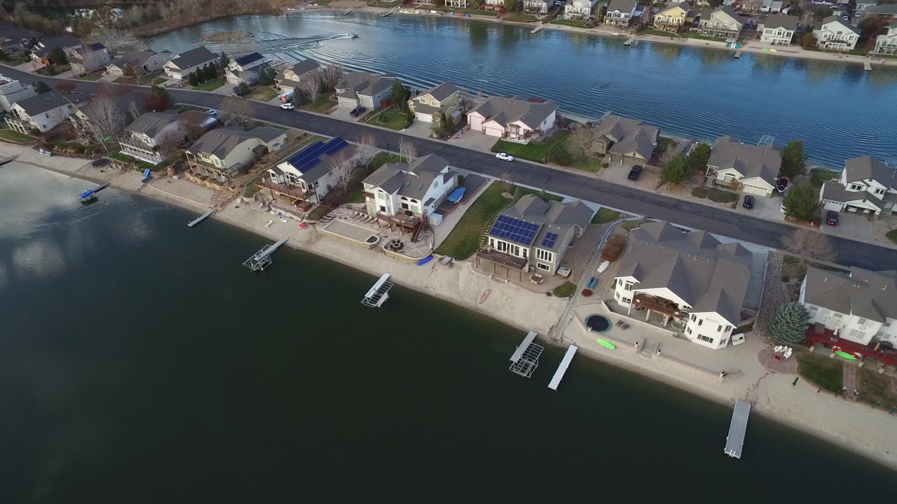 Aerial view of homes along a lake with docks and a shoreline road.