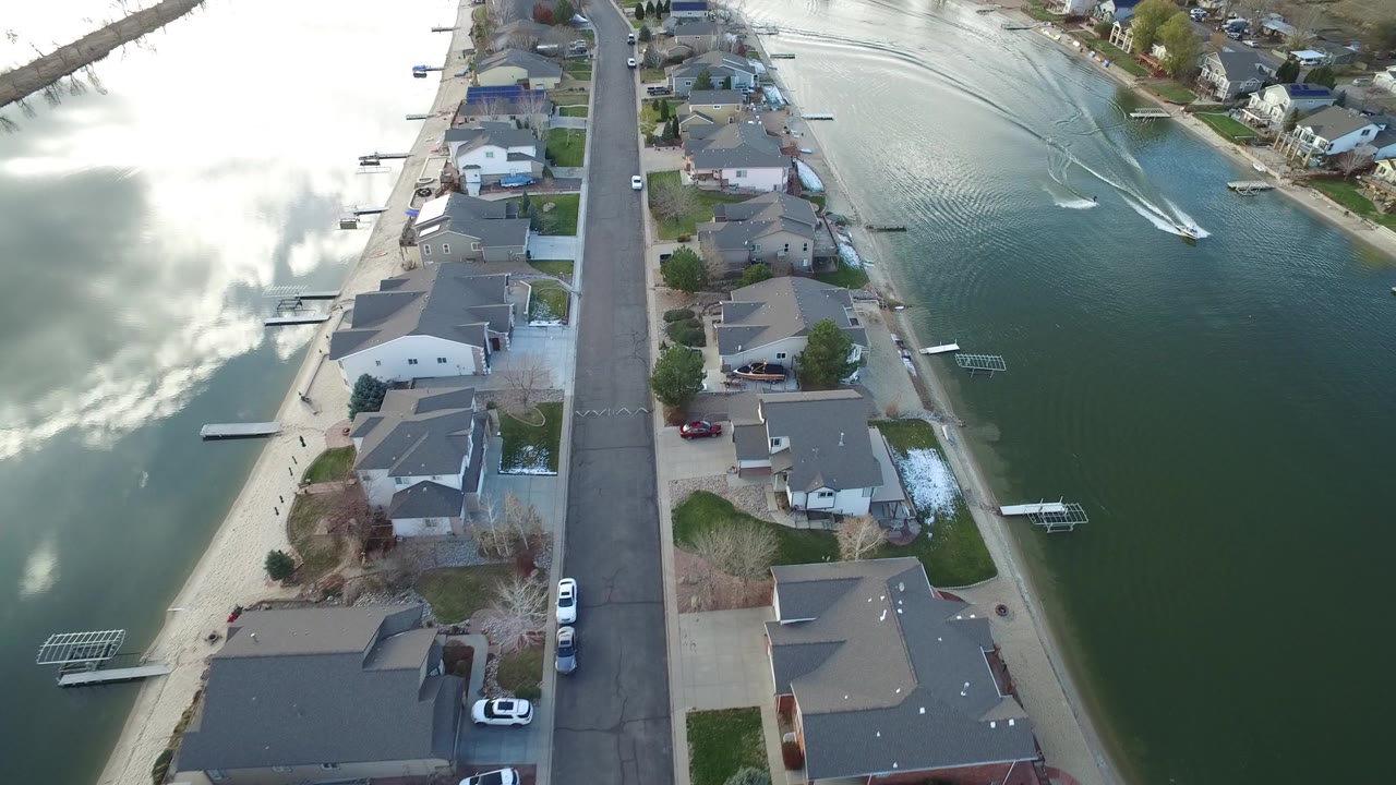 Aerial view of homes beside green water with a white boat wake.
