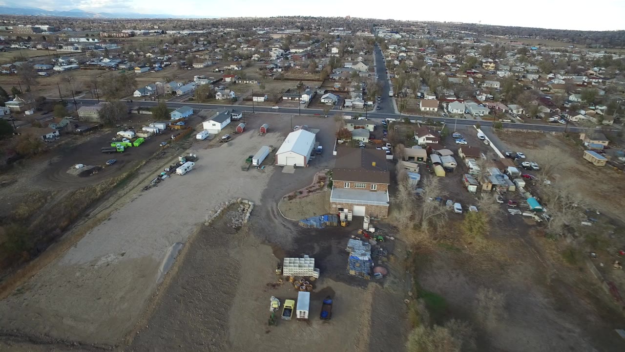 High aerial view over suburban houses, roads, gravel lots, and parked vehicles.