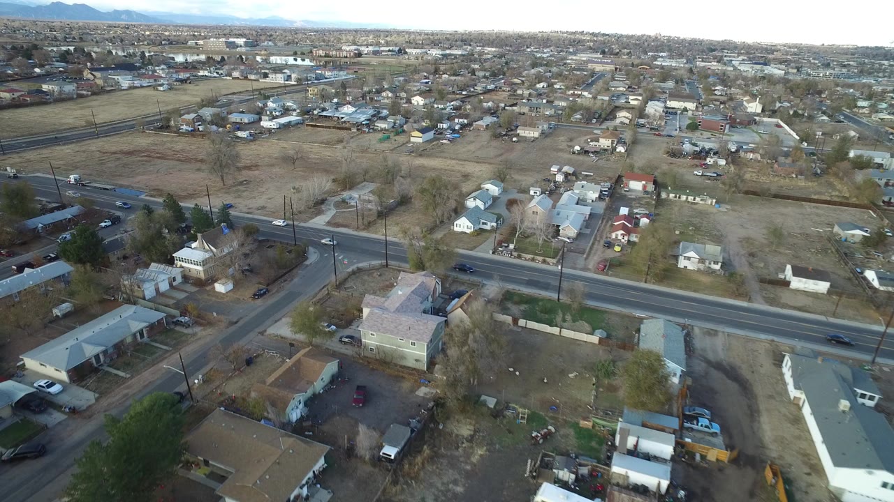 Aerial view of suburban homes, roads, open lots, and distant mountains.
