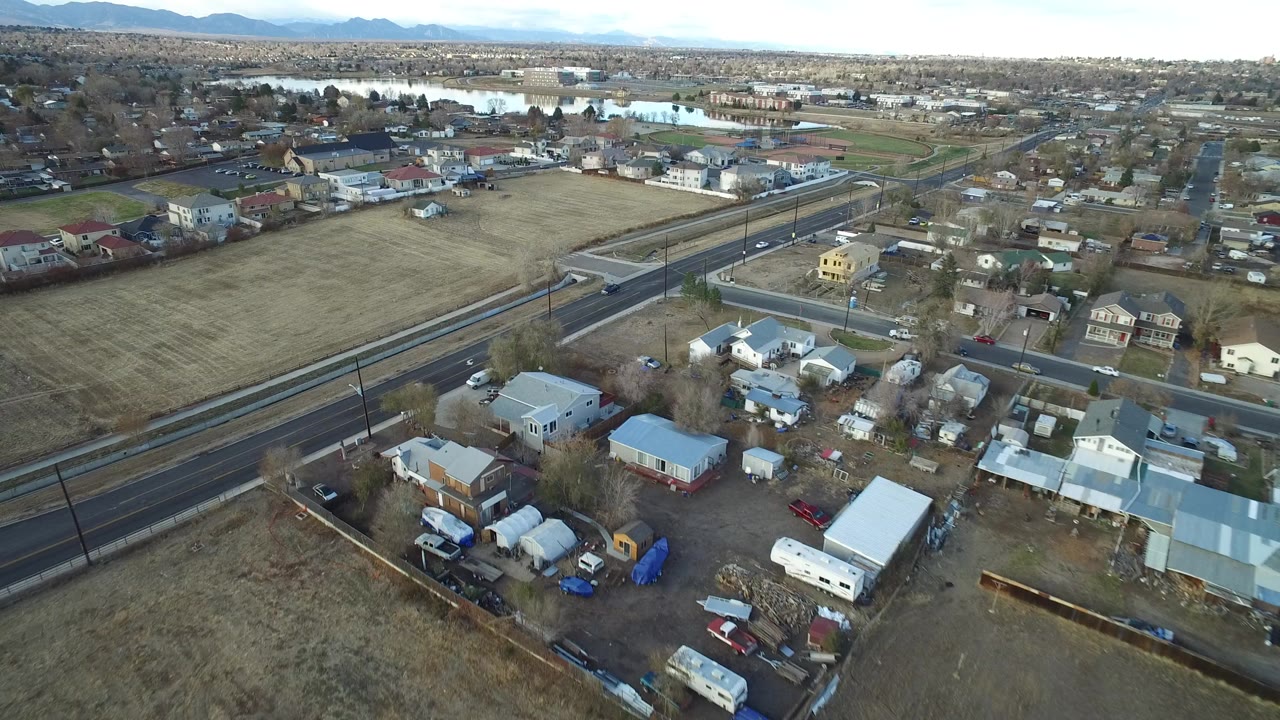 Aerial view of a suburban road, homes, open field, distant water, and mountains.
