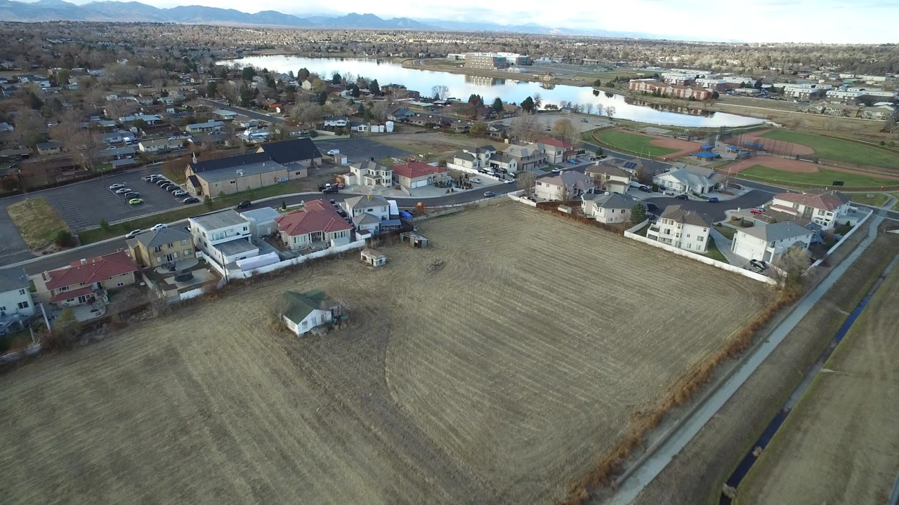 Aerial view of suburban homes, a field, a lake, and distant mountains.