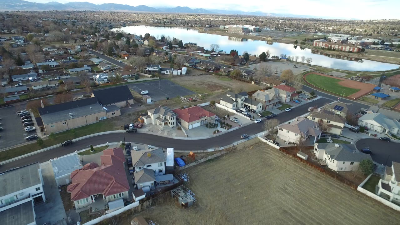 Aerial view of suburban homes, streets, a lake, and distant mountains.