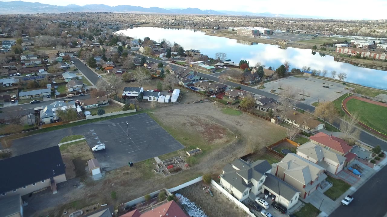Aerial view of houses, parking lot, streets, and a lake beyond the neighborhood.