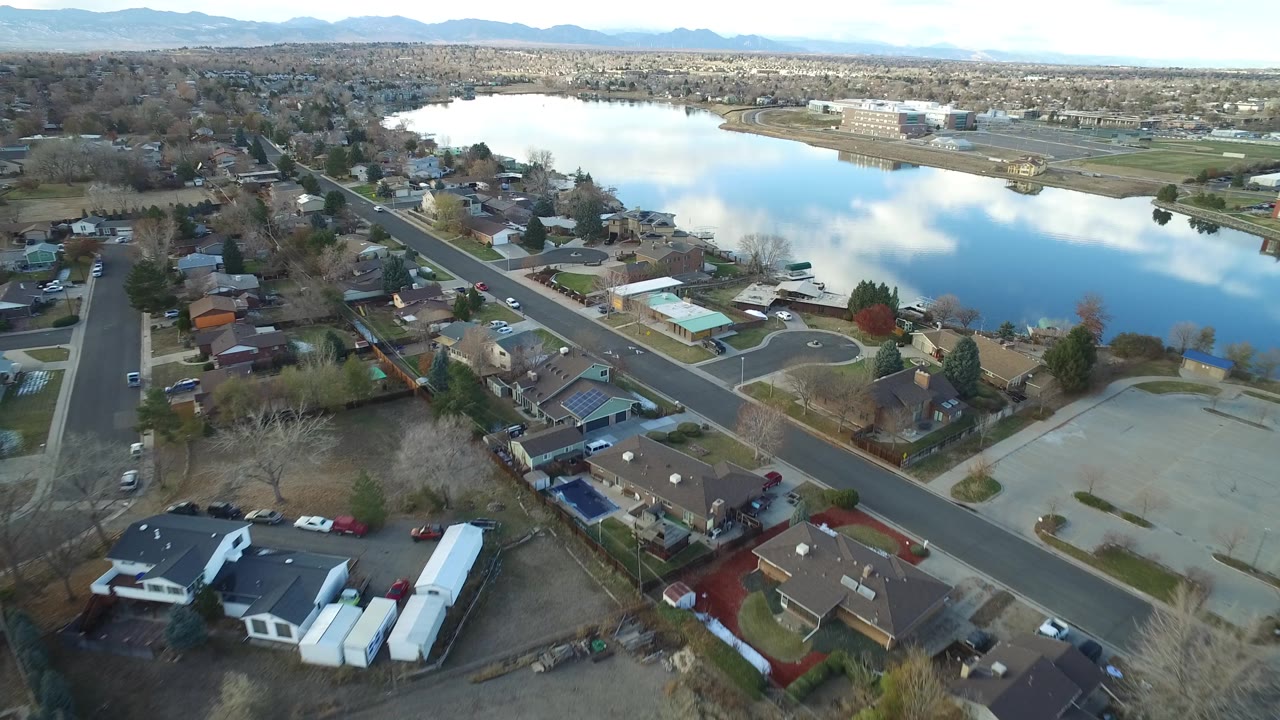 Drone-style view of a lakeside neighborhood and distant mountains.