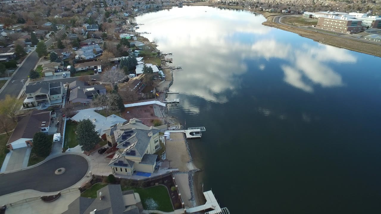 Aerial view over Westminster, Colorado waterfront homes beside a calm lake with cloud reflections on the water and no visible people.