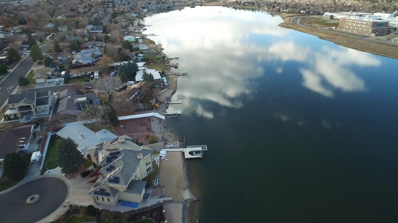 Aerial lake view with homes, docks, and a road along the far bank.