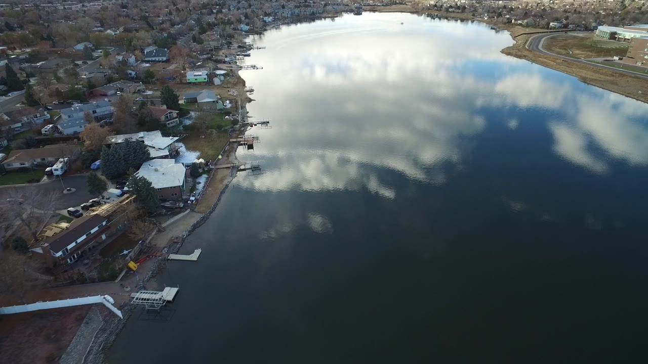 A Westminster, Colorado aerial frame centers on the reflective lake while houses, docks, and leafless trees line the left shoreline, with no visible people.