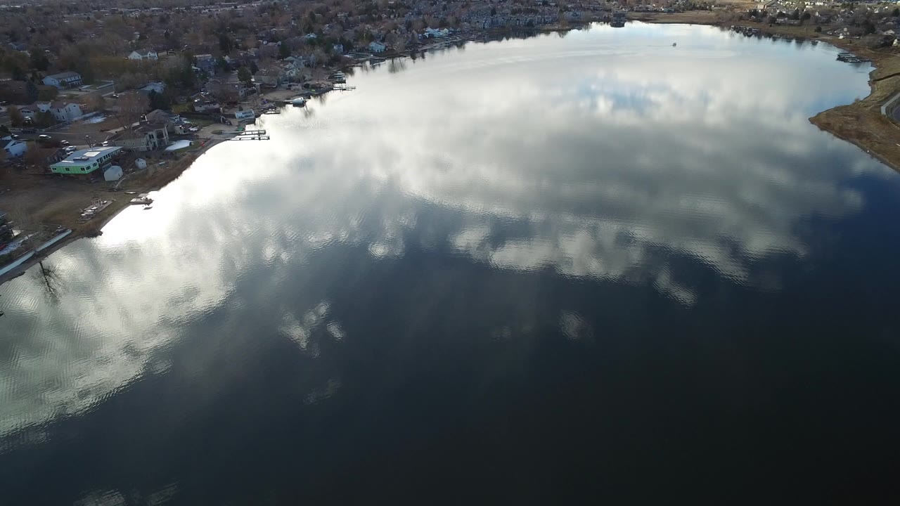 Aerial view of a lake reflecting clouds with homes along the shoreline.