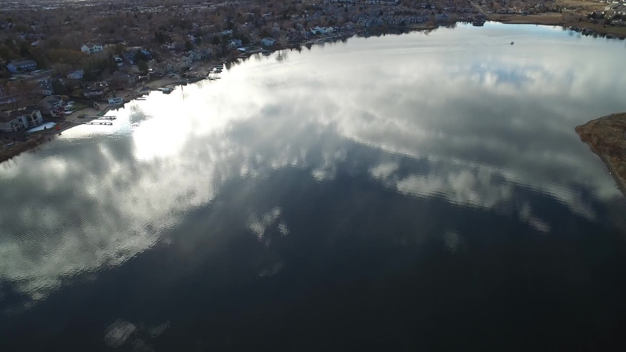 Aerial pond view with cloud reflections and a small point of land at the right edge.