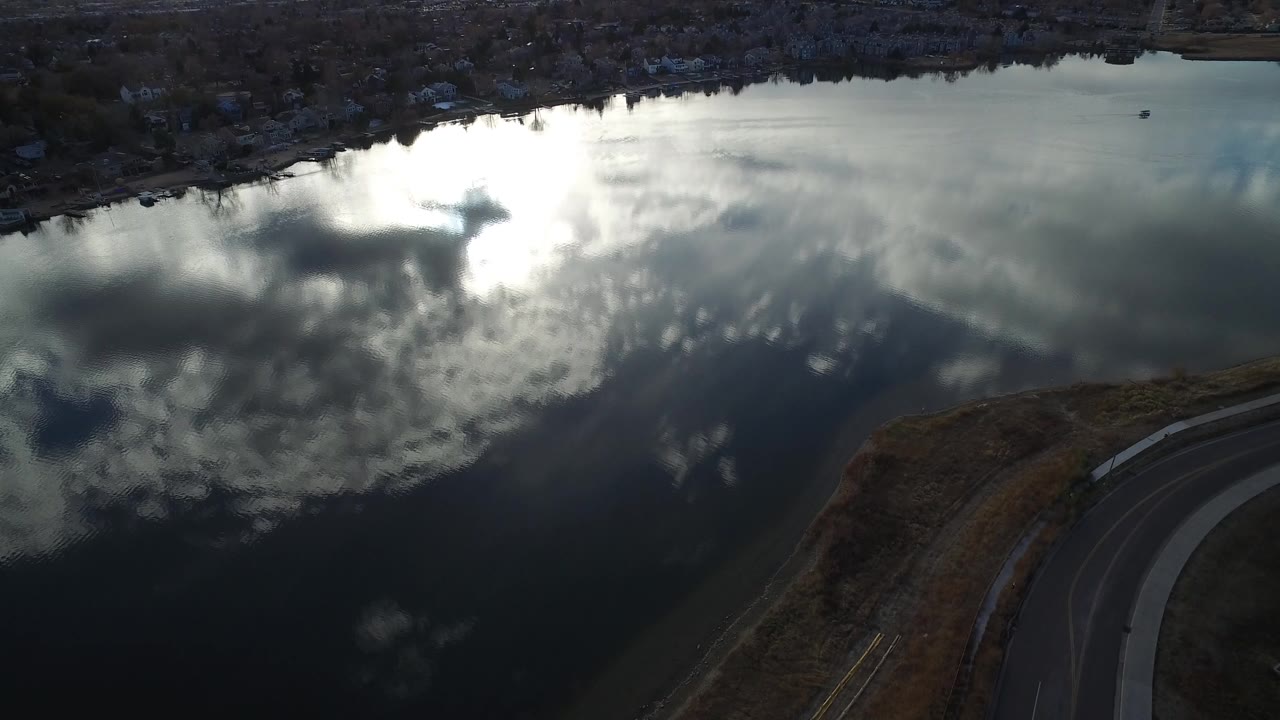 Aerial view of dark river water reflecting clouds beside a curved road