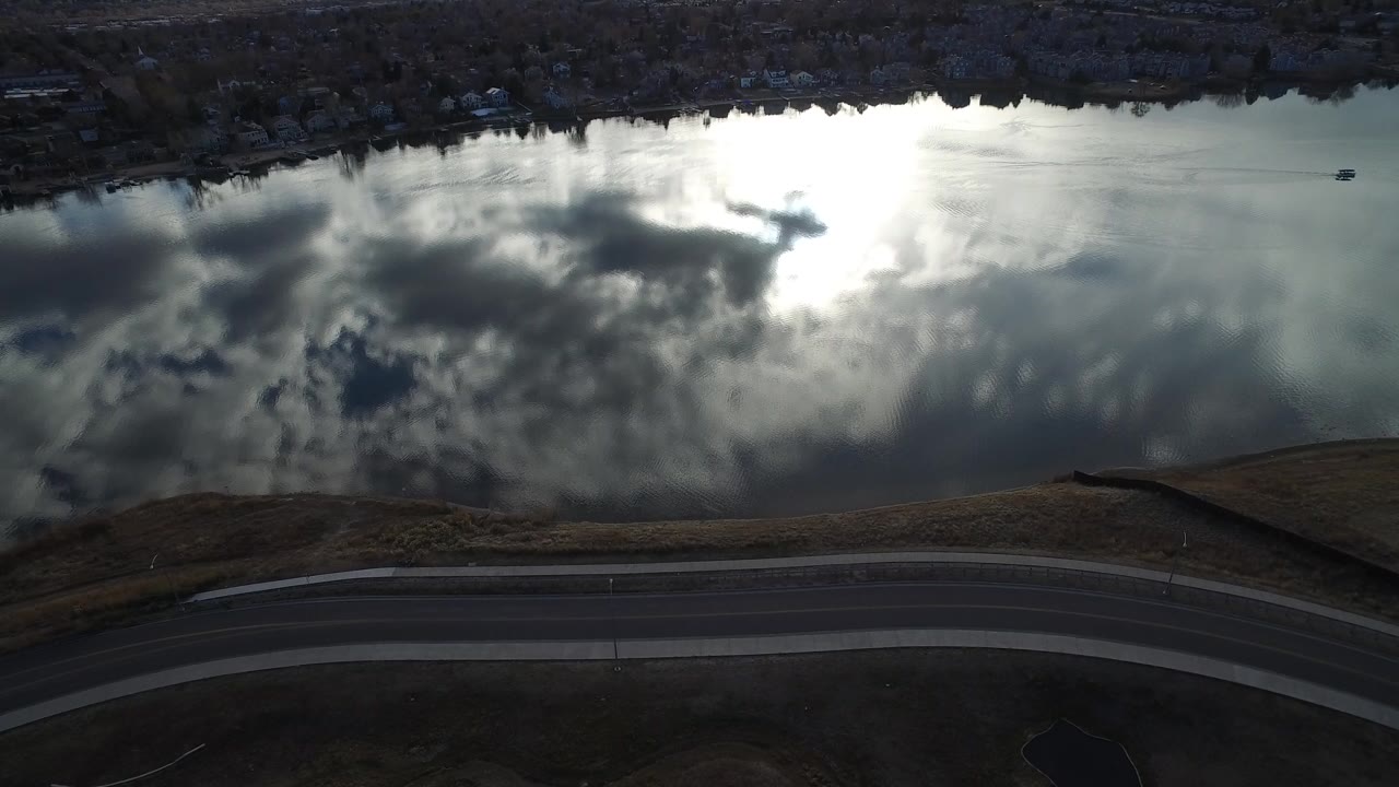 Aerial view of a lake reflecting bright clouds beside a curved road.
