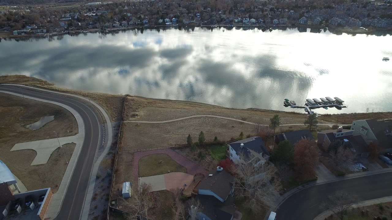 Drone view of a curved road beside a reflective lake and residential houses.
