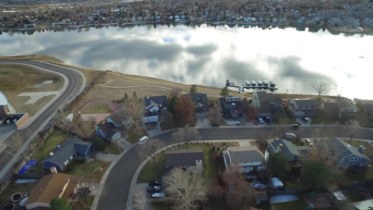 Aerial view of suburban houses and a lake under bright clouds.