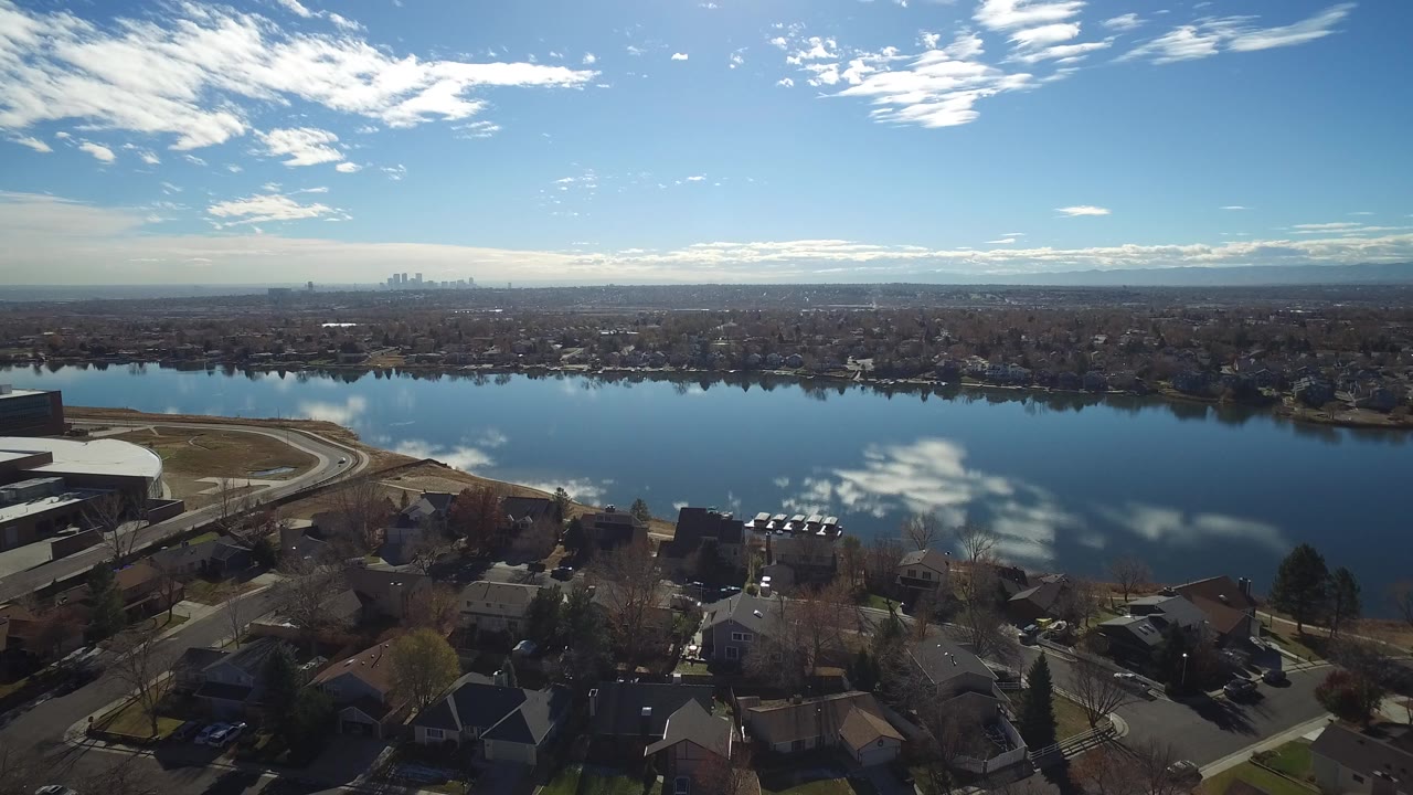 Aerial view of blue water reflecting clouds beside suburban homes.