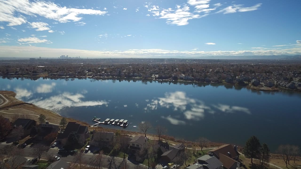 Wide aerial view of a lake with houses, dock slips, clouds, and distant skyline.