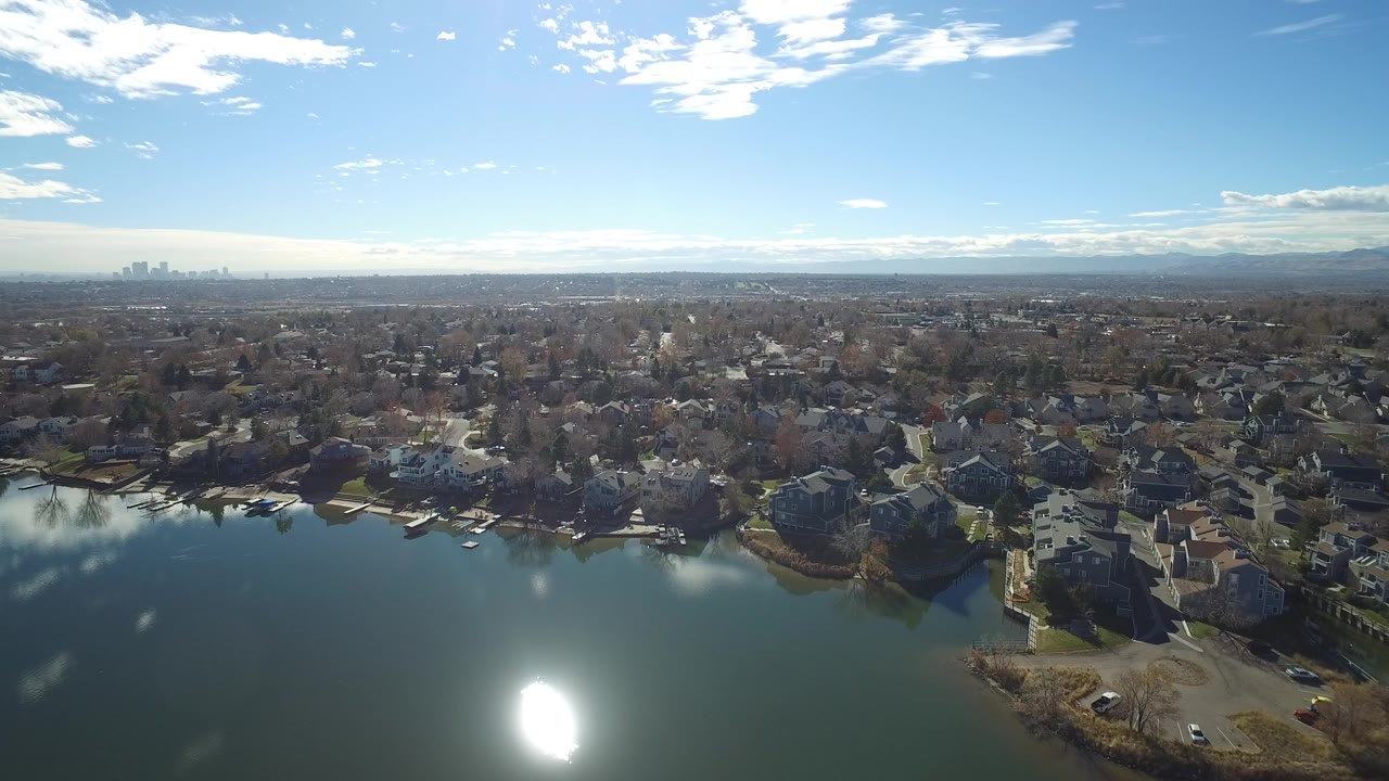 Aerial view over a lake and suburban homes under a blue sky.