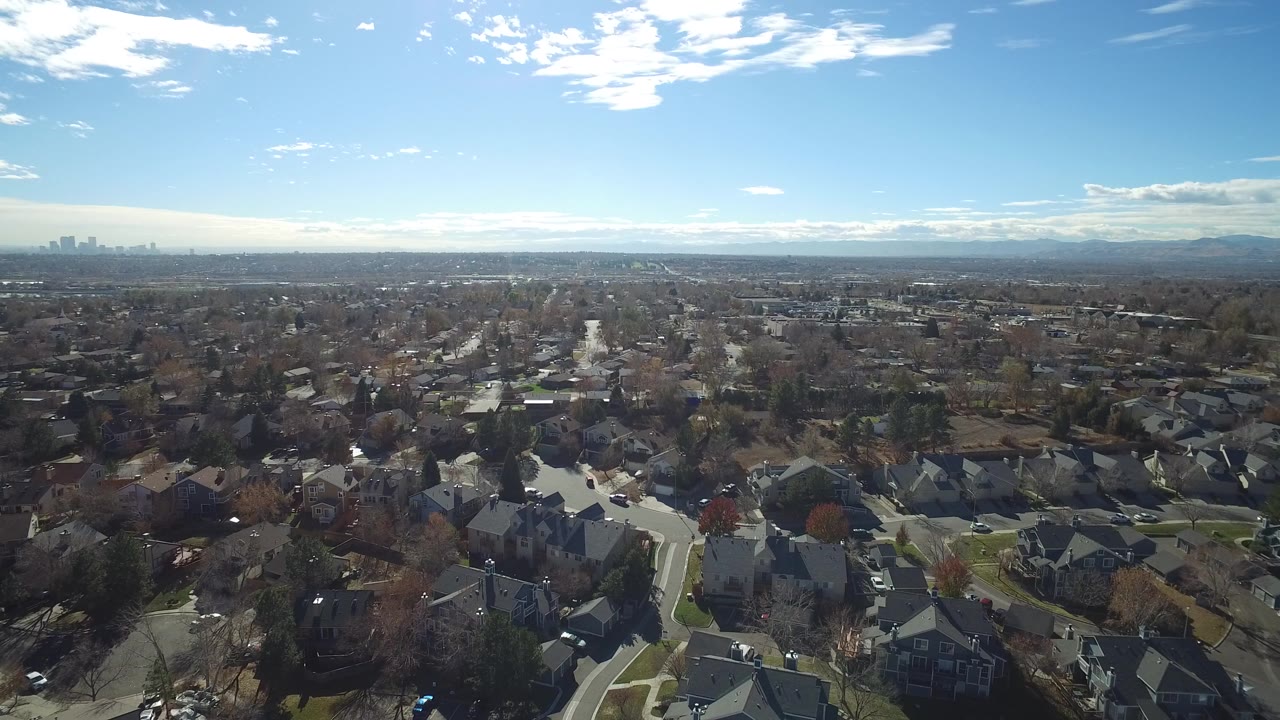 Aerial view over suburban houses and streets under a blue sky.