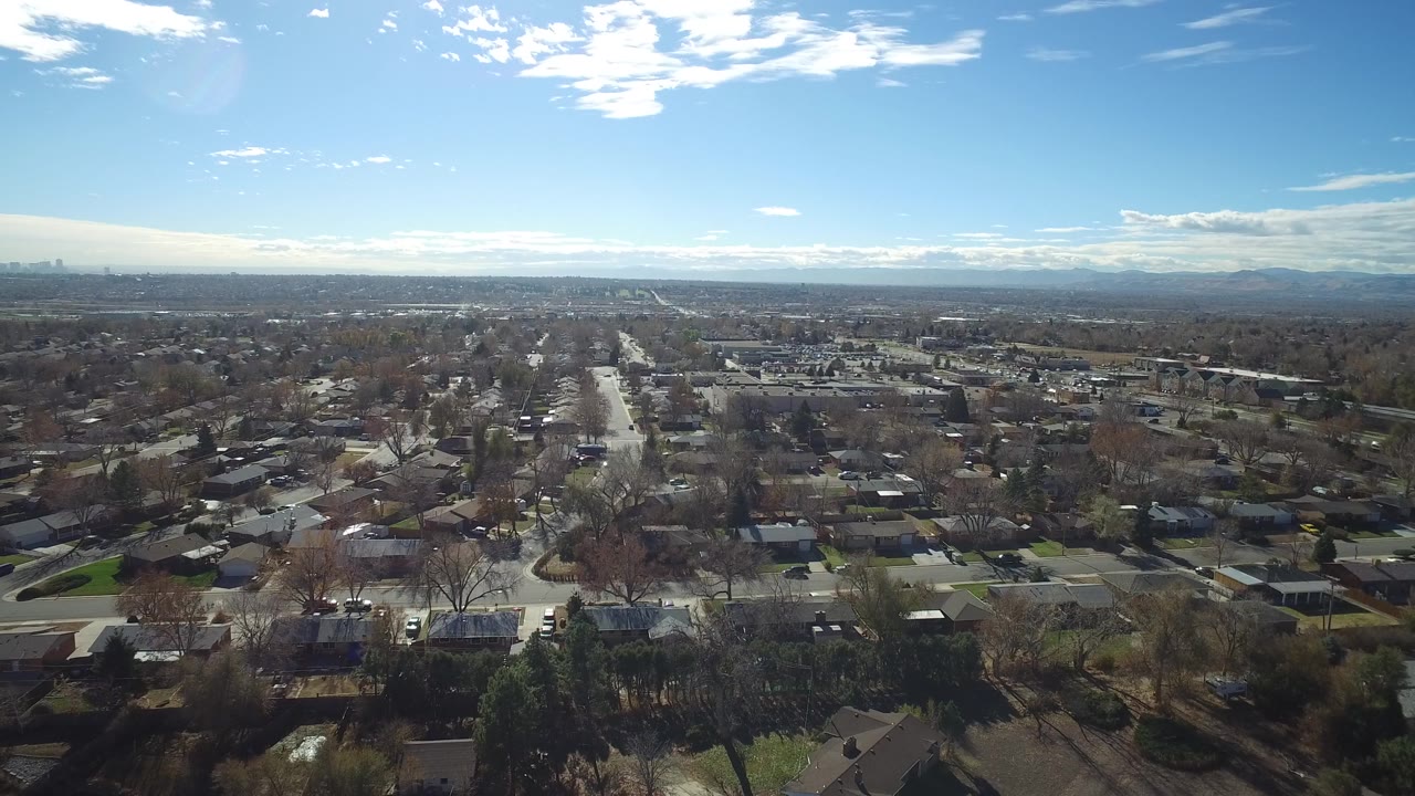 Wide aerial view over suburban streets and houses beneath a blue sky.