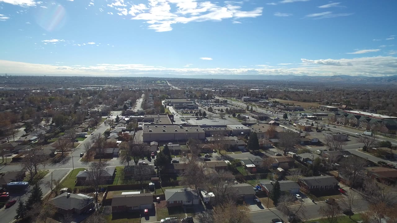 Aerial view over suburban streets, rooftops, low buildings, and blue sky.