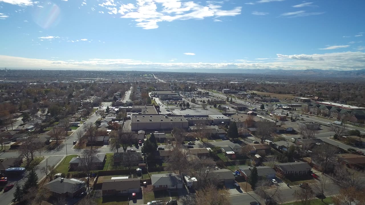 Aerial view in Westminster, Colorado, with private homes in the foreground, a parking lot and low buildings in the midground, mountains on the horizon, and no visible people.