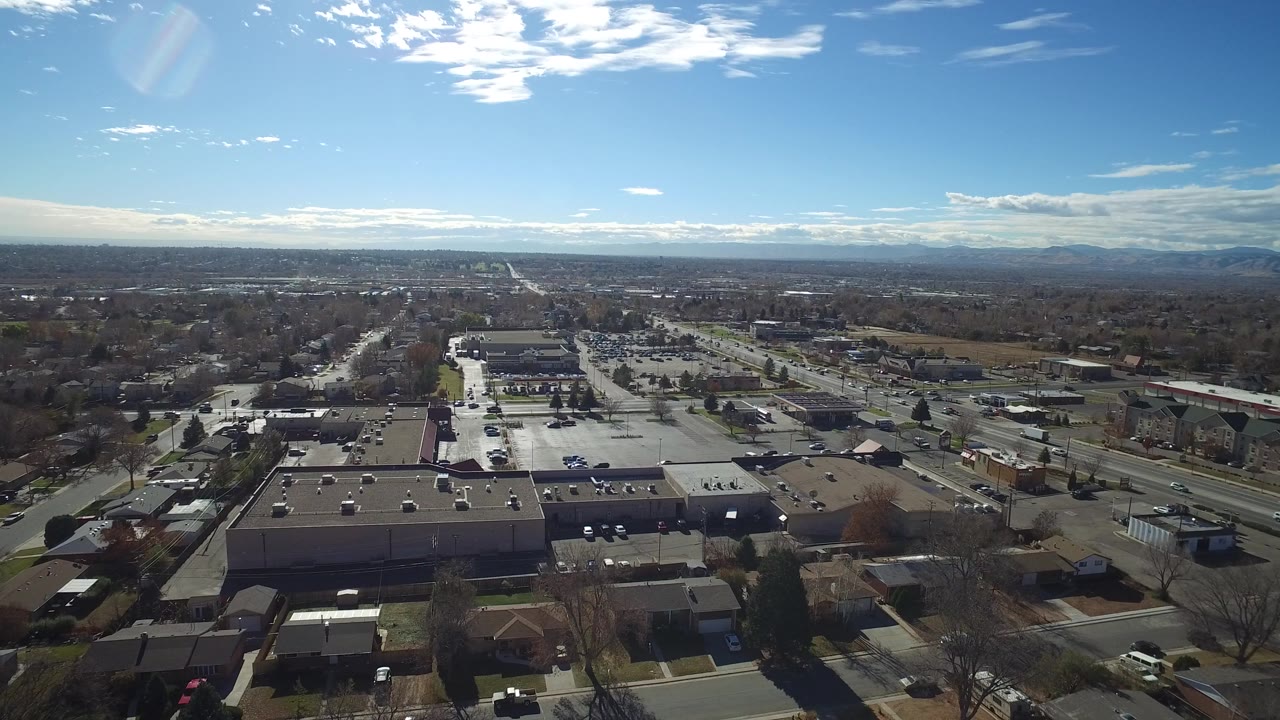 Aerial view over commercial buildings, roads, parking lots, and distant mountains.
