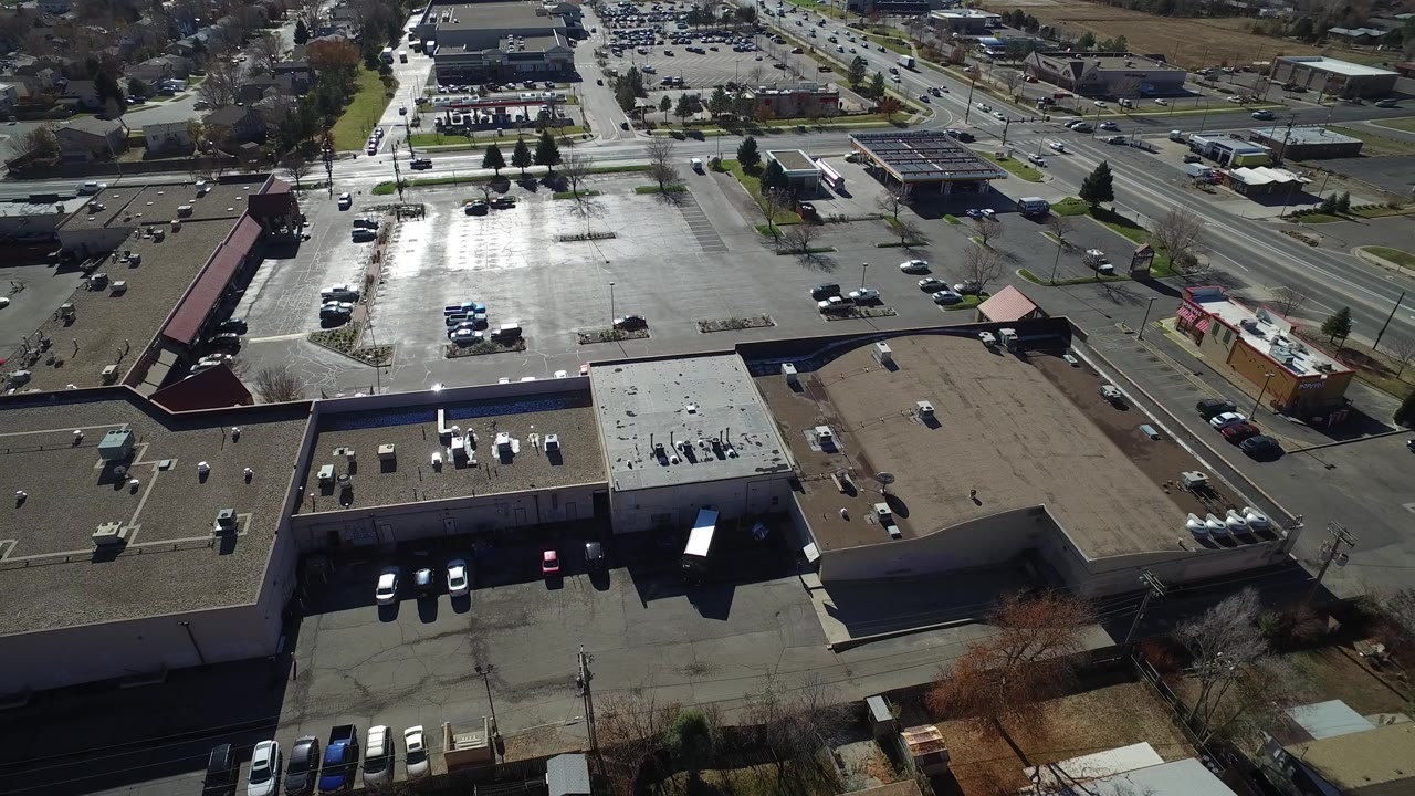 High oblique view across storefront buildings, a bright parking lot, and suburban streets.