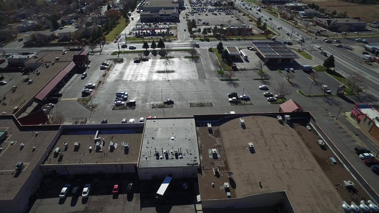 Aerial view over commercial rooftops, a parking lot, and a busy road.