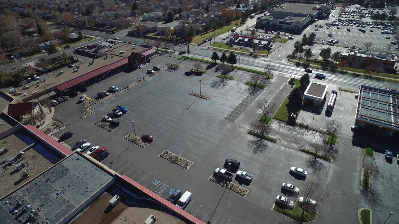 Aerial view of a mostly empty parking lot beside low commercial buildings.