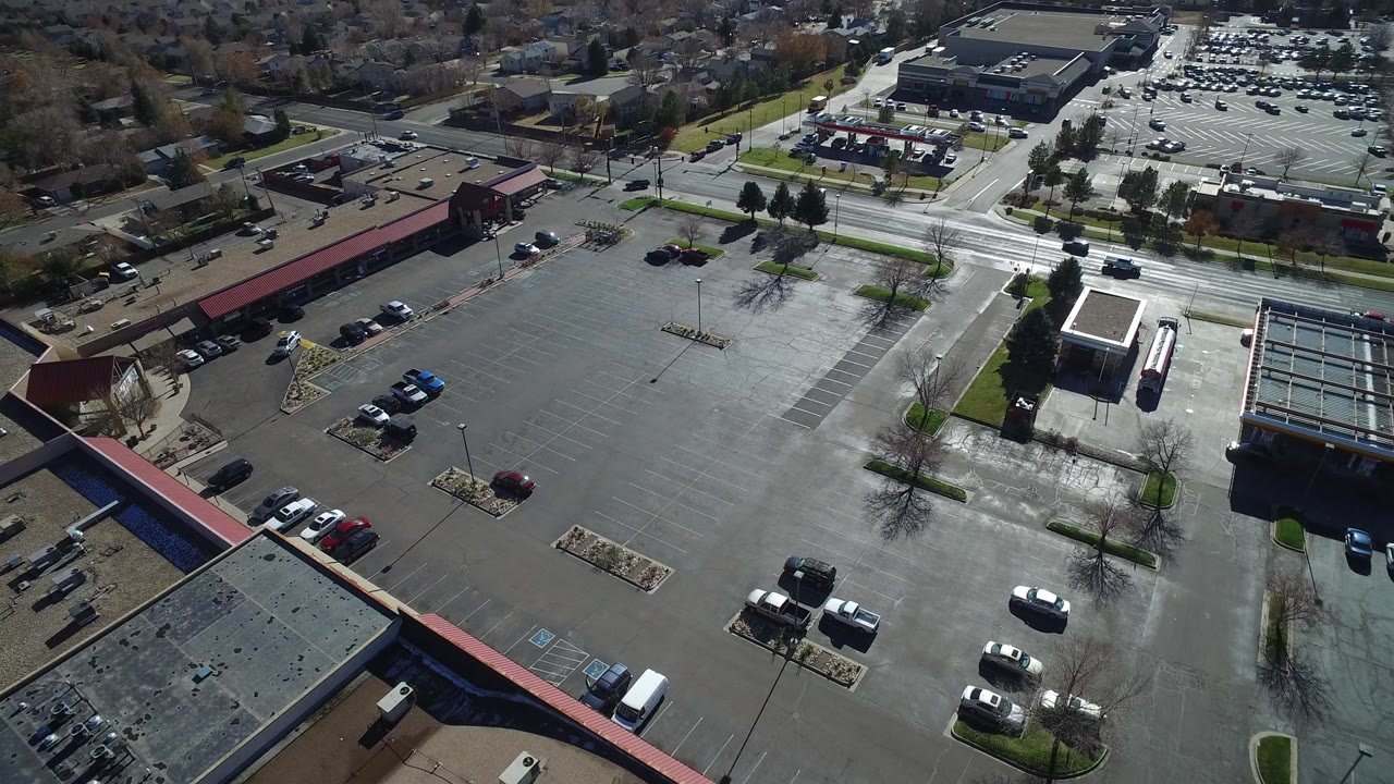 The second frame keeps the Westminster, Colorado parking lot centered, with a glass-roofed building at lower right, parked cars at the edges, cross streets beyond, and no visible people.