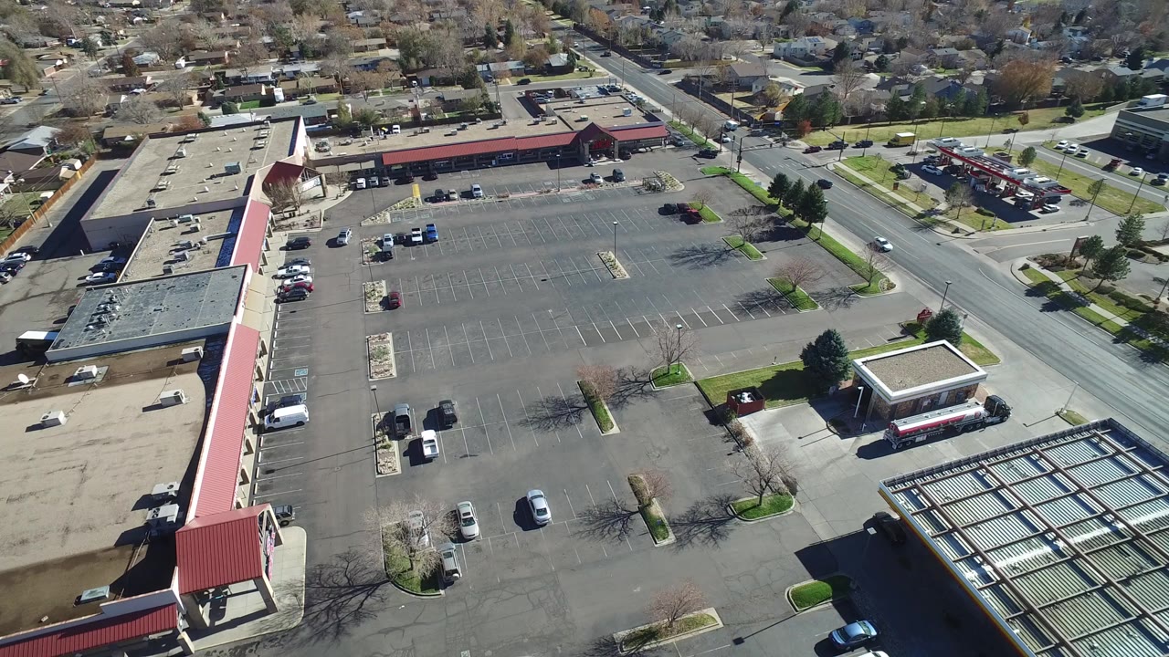 Aerial view over a suburban parking lot and retail buildings.