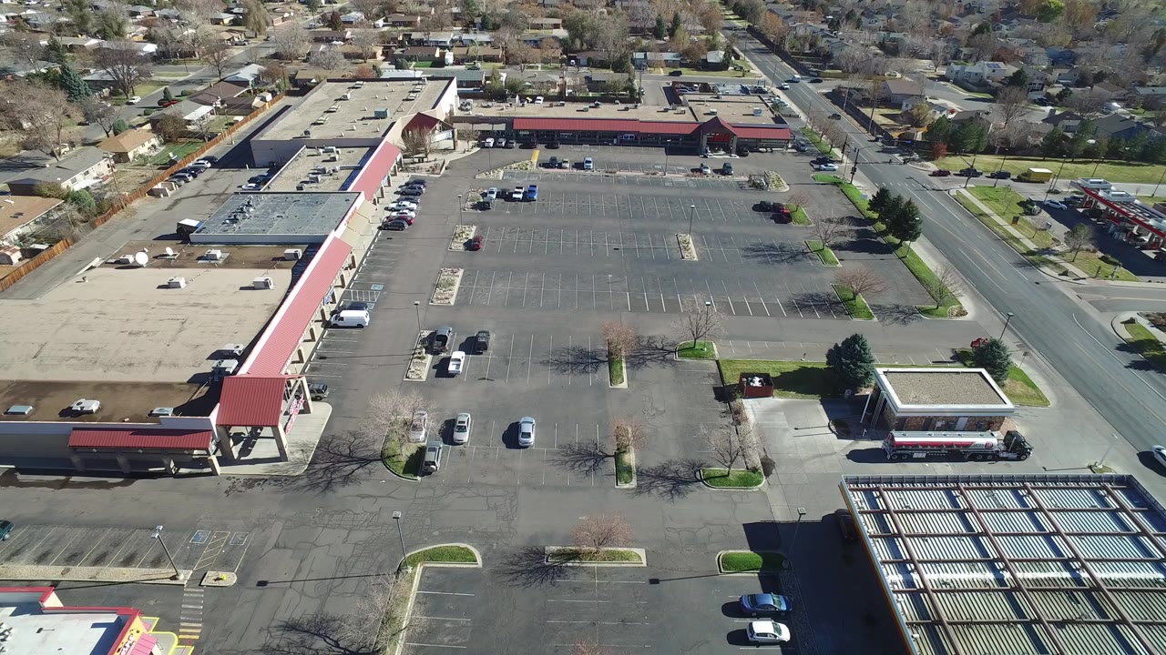 Aerial view over a large suburban parking lot beside low commercial buildings.