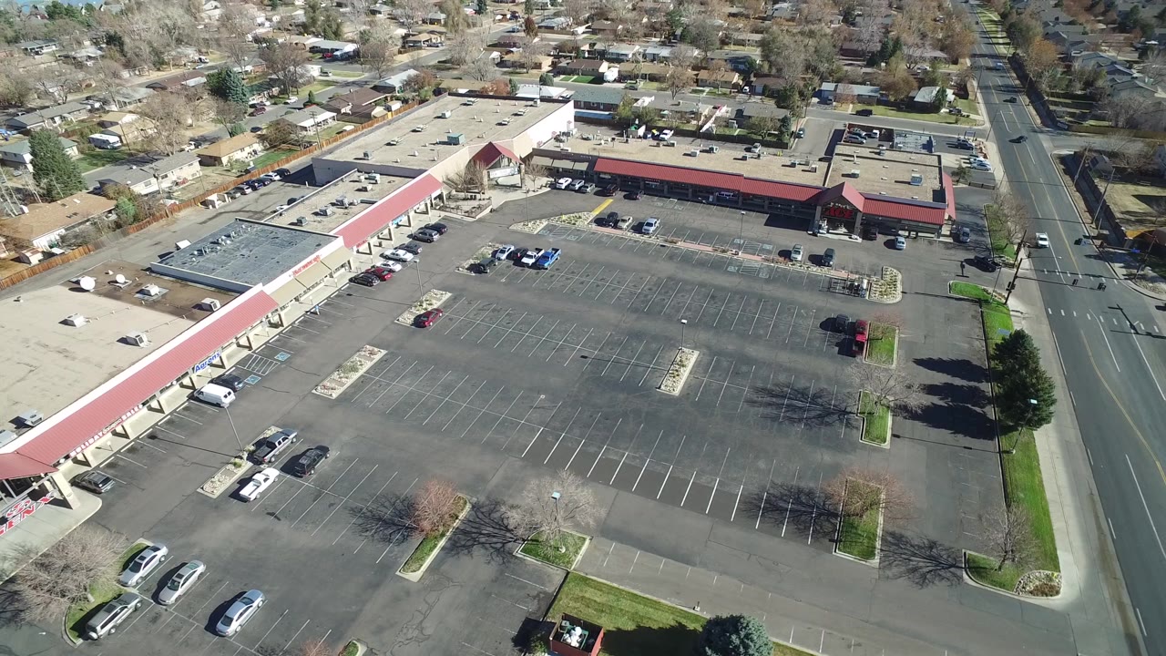 Drone view of a mostly empty parking lot with a retail building and road at right.