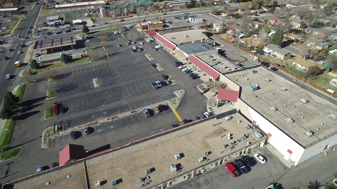 Aerial view over a Westminster, Colorado commercial parking lot with red awnings, parked cars, surrounding roads, nearby houses, and no visible people.