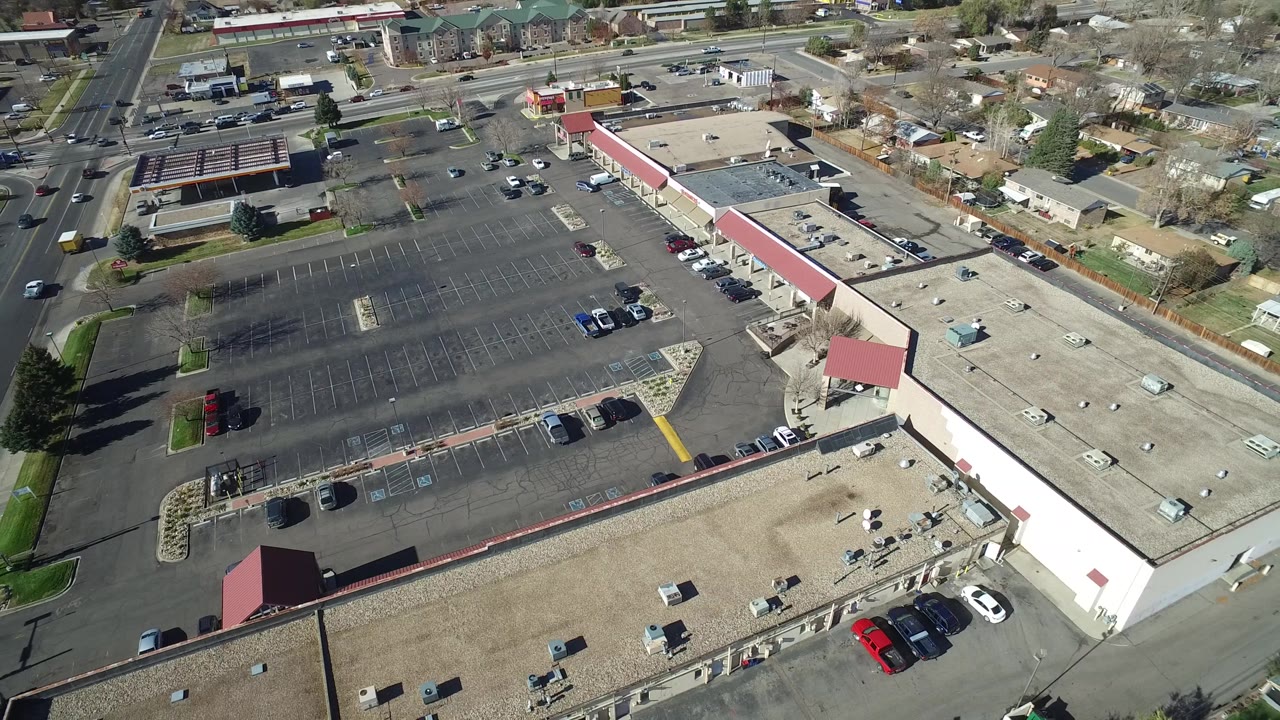 Second overhead frame in Westminster, Colorado showing the same mostly empty parking lot, long beige roof, red awning corners, parked cars, and no visible people.