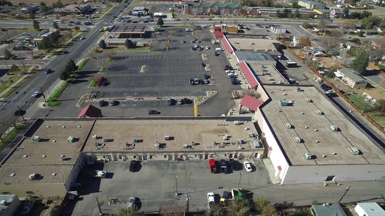 Aerial view of a commercial building, parking lots, roads, cars, trees, and houses.