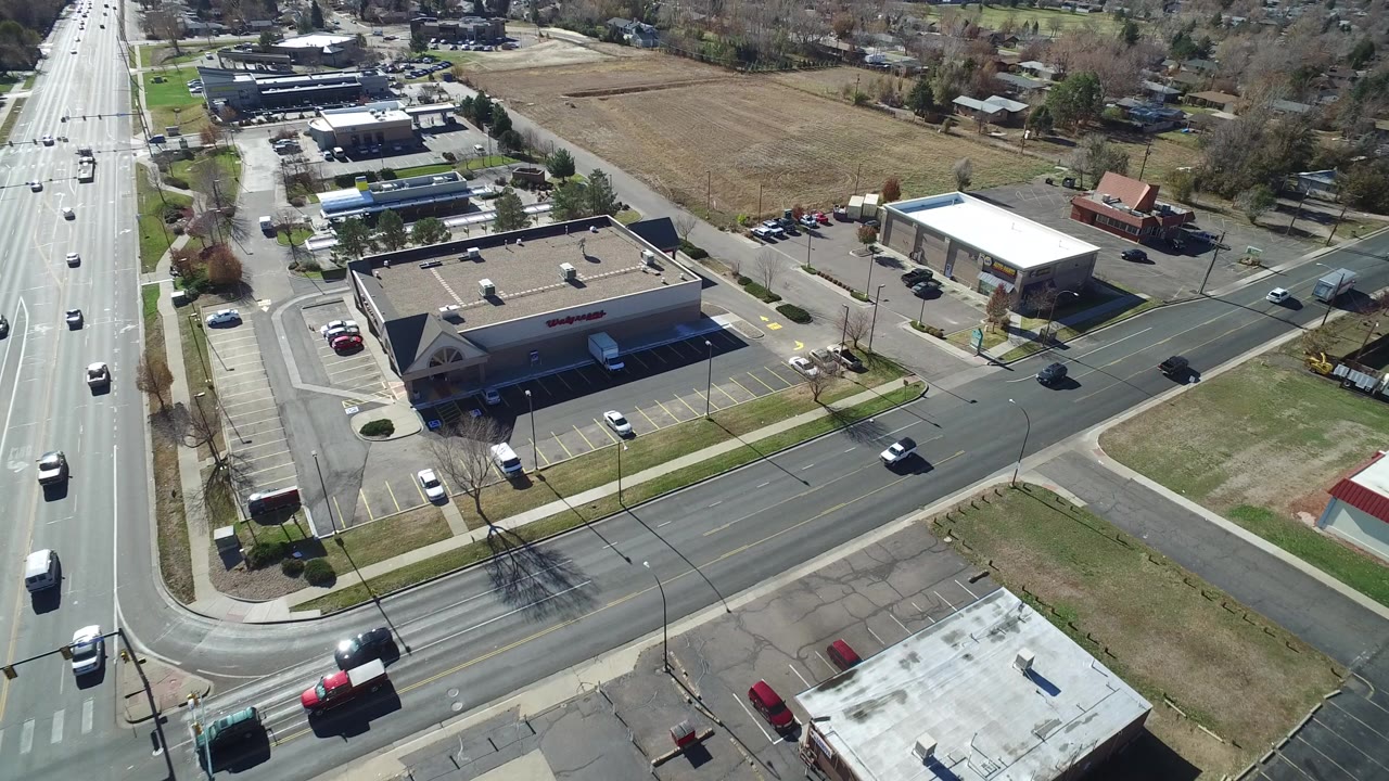 Aerial view of a road intersection, retail building, parking lots, and open land.